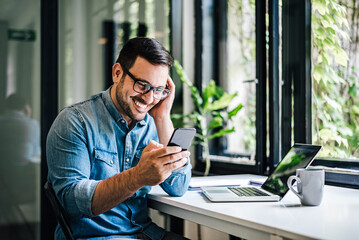 Portrait of young smiling happy handsome successful businessman entrepreneur freelancer working from office using smart phone