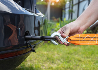 A man's hand clings a tow rope to a tow hook in a passenger car, close-up. Summer