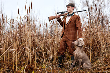 Hunting period, autumn season open. confident young caucasian hunter with dog and gun in brown...