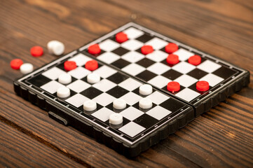 A board for playing checkers with chips on a wooden table, close-up, selective focus.