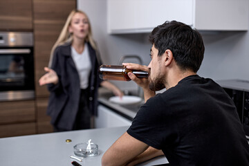 Family quarrel. Unhappy young caucasian family during conflict in kitchen at home. Focus on male drinking alcohol beer. Married couple arguing, male is ignoring, looking at side.