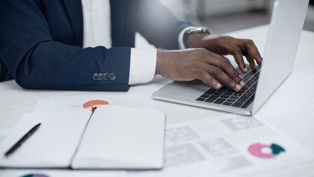 partial view of african american businessman using laptop near charts on desk.