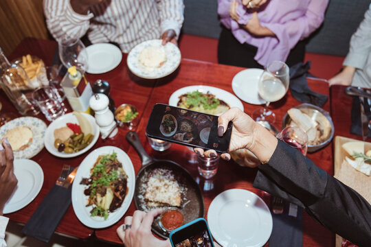 Cropped image of woman photographing on smart phone while having dinner with friends at bar