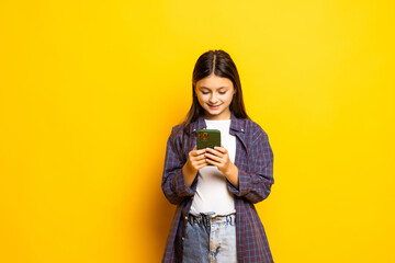 Excited caucasian kid girl over yellow background winking and eye hold smart phone use read social network news