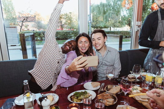 Woman taking selfie with male friends while celebrating in bar afterwork