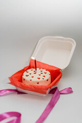 Woman holding Bento Cake for Valentines day with candle. Portioned trandy dessert for one person in eco box with purple ribbon, small cake. Pink ribbon.