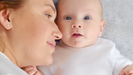 Happy newborn baby with his mother. Healthy newborn baby in a white t-shirt with mom. Closeup Faces of the mother and infant baby. Cute Infant boy and parent, top view. Happy family portrait