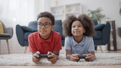 Two happy african american kids playing video game with joysticks, home leisure