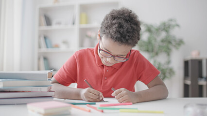 Happy black boy drawing with color markers, sitting at the table at home, hobby