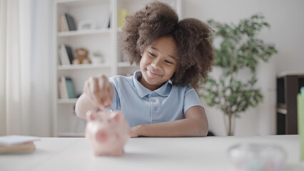 Little girl putting coin into pink piggybank, child learning to save money