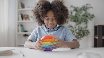 African American girl playing with pop it toy, pressing buttons, stress relief