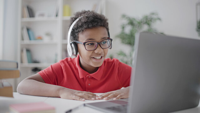Pupil in headphones smiling looking at laptop display, learning online, distance education