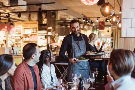 Waiter serving food to multiracial customers during party in restaurant