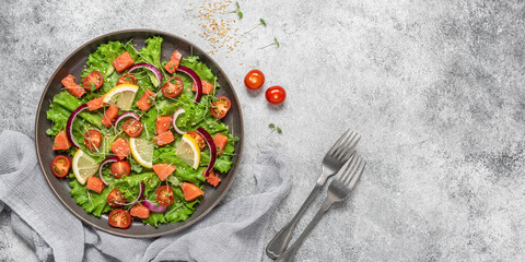 Fresh salad with salmon, tomato, lettuce leaves, microgreens, red onion and sesame seeds. Gray concrete rustic background. Top view, flat lay, banner