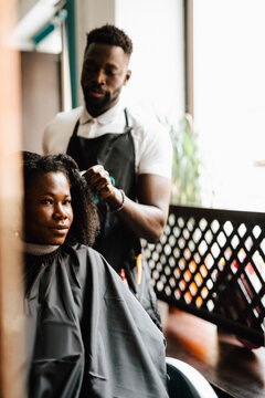 Male hairdresser cutting hair of female customer in barber shop