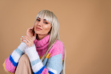 A blonde with long hair and bangs, with nude makeup and in a multi-colored bright fluffy sweater on...