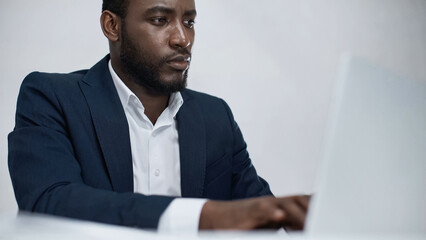 african american businessman using blurred laptop isolated on grey.