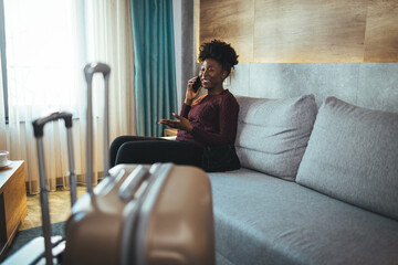 Close-up of luggage and blurred background of a happy tourist woman in a hotel after check-in. The concept of travel and vacation. She reports that she arrived safely via her smartphone