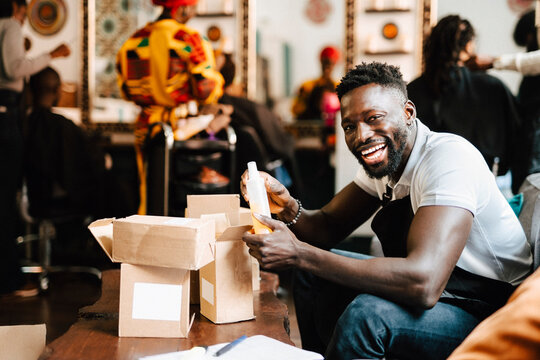 Cheerful male barber packaging beauty product in box at hair salon