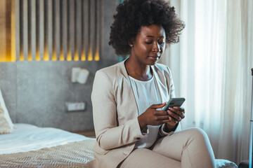 Young black businesswoman just arrived at the hotel taking a rest from a trip, using a smartphone....