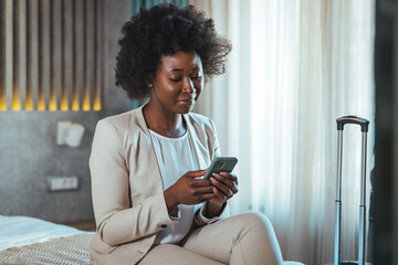 Young black businesswoman just arrived at the hotel taking a rest from a trip, using a smartphone....