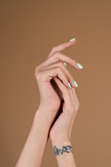 Graceful female hands with thin long fingers and mint turquoise manicure on a beige background