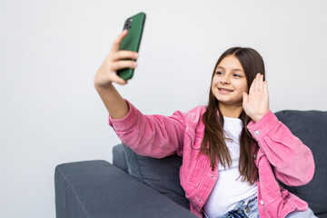 Portrait of attractive cheerful girl influencer blogger sitting on sofa taking selfie video streaming free time at light flat home