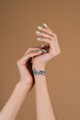 Graceful female hands with thin long fingers and mint turquoise manicure on a beige background