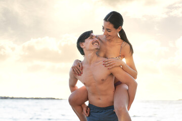 Photoshoot of young beautiful couple, boy and girl, dating at the beach, she on his shoulders - Man and woman lovers standing near the ocean in a sunny day