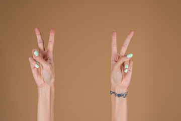 Women's hands on a beige background, show a victory gesture V