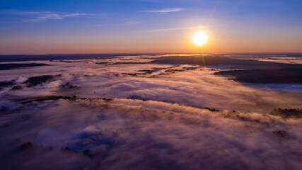 Fototapeta na wymiar Aerial view of a beautiful summer landscape with a fog while dawn. Photo from drone of a foggy landscape in spring. Top view to land while sunrise. Sun is above the horizon