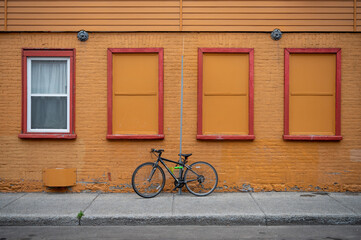 Fototapeta na wymiar A Bicycle Rests Locked Up To A Thin Post With A Yellow Brick Building With Four Windows Behind It. 