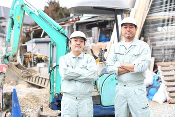 工事現場の重機の前で腕組みをする作業員の男性達（カメラ目線）
