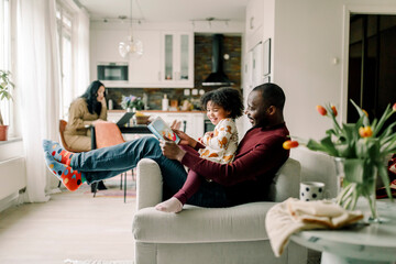Smiling father teaching daughter sitting on chair in living room