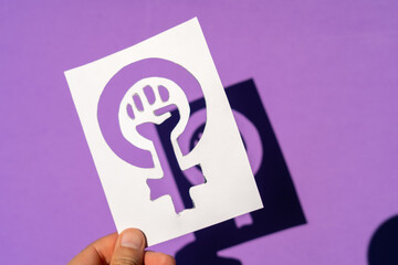 Symbol of the struggle of feminism on a purple background, clenched fist of a woman in the march...