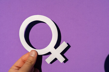 A woman holding the female symbol on a purple background, march for women's rights and equality