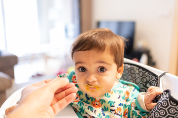 Father feeding his baby solid food, his first vegetable purees, first person view of the father feeding him spoonfuls at home