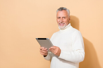 Portrait of attractive cheerful grey-haired man using device blogging app smm isolated over beige pastel color background