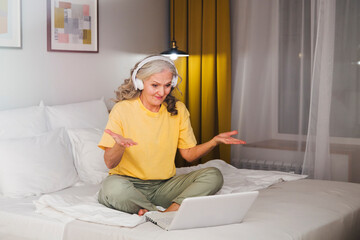 healthy seniors lifestyle. work from home. elderly woman in headphones communicates online or watching video on a laptopin the bedroom of the house. 