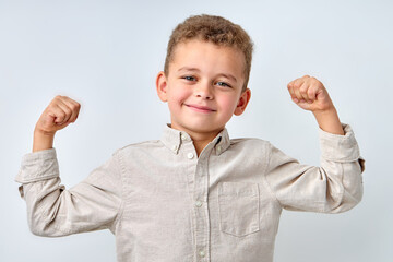 Handsome confident child boy in casual shirt smiling happily and raising clenched fists, tensing muscles, feeling strong and full of energy after ate healthy protein lunch. isolated on white