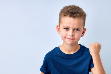 handsome boy looks angry. The child is offended, threatens, shows a fist. Angry, resentful, aggressive child. Portrait on white studio background. Children's human emotions concept