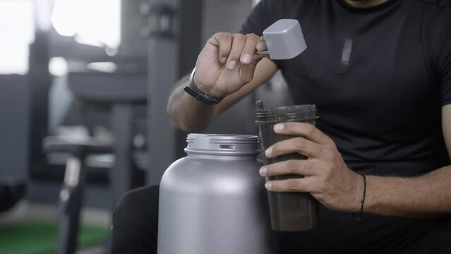 close up shot of bodybuilder hands taking protein powder and mixing with water on bottle by shaking at gym - concpet of muscular gain, nutritional supplement and wellness