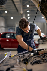 concentrated auto mechanic male working alone repairing engine of the car in hood, looking at...