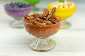 Smoothie or pudding with chocolate, hazelnuts and almonds served in a bowl for breakfast with several other smoothies in background