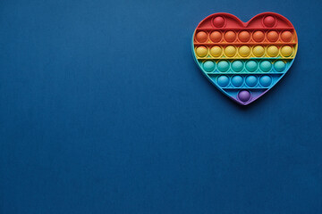 Heart, silicone rainbow anti-stress toy on  blue background. Click on pop-up bubble,  simple dimple...