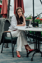 Smiling young dark-haired businesswoman makes notes in a notebook in a cafe on a summer day. Business, e-learning, freelance concept. laptop on a table