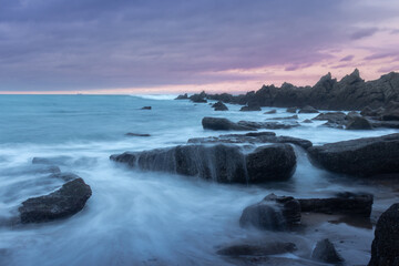 Fototapeta na wymiar Anocheciendo con un cielo magico sobre un mar sedoso que fluye entre las rocas