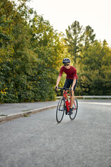 young healthy caucasian man dressed in sportive cycling clothes outfit riding bicycle on asphalt out-of-town path. handsome guy is engaged in sport. Active sporty people concept image.