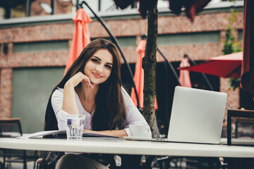 Young freelancer woman using laptop computer sitting at cafe table. Smiling woman working online or studying and learning while using notebook.