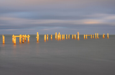 A minimalism slow shutter exposure of Swanage Dorset  bright orange old pier posts in a still grey sea